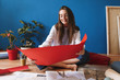 Smiling girl sitting on floor holding red whatman paper in hands while happily spending time at cozy home