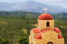 Greek Church On The Blurred Background Of Green Olive Plantations And Blue Mountains