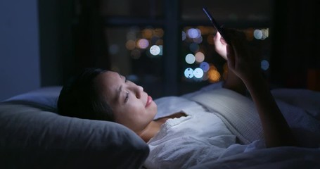 Wall Mural - Woman use of mobile phone and lying on bed at night