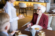 © Seventyfour - Elegant senior woman making an order to waitress while sitting at the table and eating together with young man