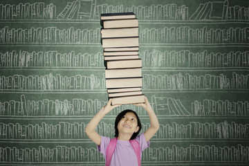 Wall Mural - Asian schoolgirl lifts a pile of books in the library