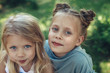 © Yakobchuk Olena - Waist up portrait of sisters sitting on grass in cuddles. They are happy and delighted to spend time outside