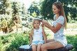 © Yakobchuk Olena - Full length of small cute child sitting on bench in park with mother beside her. Smiling woman is touching kid hair with content. Copy space in left side