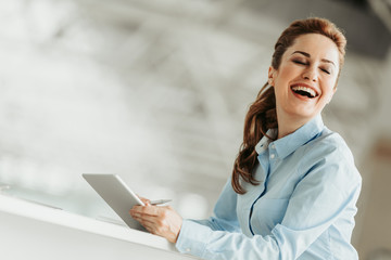 Poster - Portrait of laughing female employer with attractive smile and closing eyes using digital device during labor. Satisfied lady during labor concept