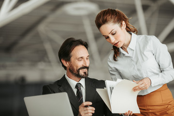 Poster - Portrait of satisfied bearded businessman speaking with concentrated female employee. They discussing documents during job