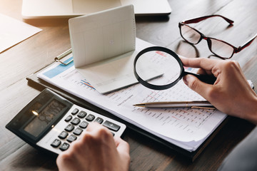 An auditor hand holding magnifying glass over saving account passbook for looking and analysis financial data,  Business finances and Saving concept.