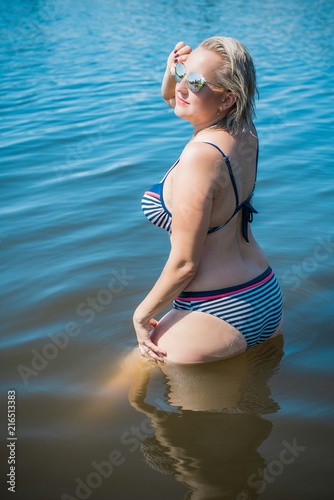 Natural pretty blonde head woman in swimsuit near water. Size plus and xl woman. Swimsuit bikini ,lady at beach. Life of plump people in everyday life, ... Natural pretty blonde head woman in swimsuit near water. Size plus ...