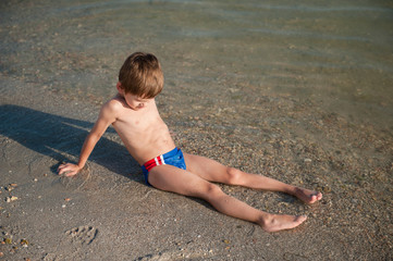 strong healthy boy sitting on sand in sea water on beach during summer vacation