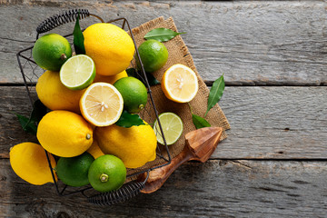 Wall Mural - Top view of lemons and limes fruits in basket on wooden background.