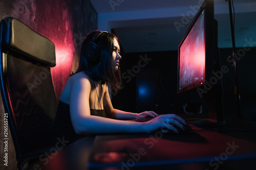 Fotografie, Obraz A cute female gamer girl sits in a cozy room behind a computer and plays games