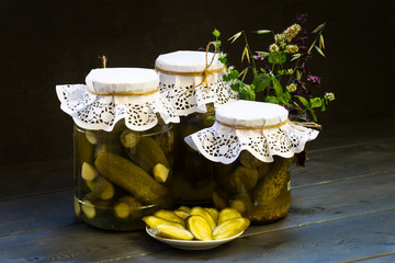 Banks with pickled or pickled cucumbers. Canned vegetables. Harvest for the winter. Wildflowers, mint, basil, oats. Dark background. Food photo.