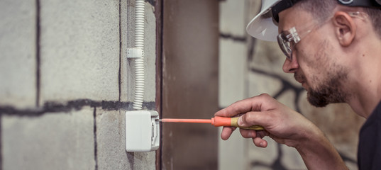 Wall Mural - male electrician-technician, connects the equipment with a tool