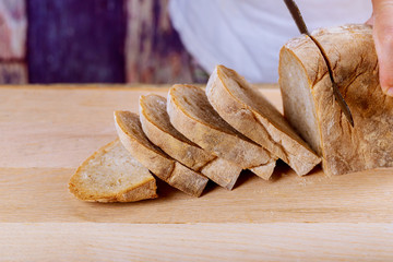 Fresh whole grain bread on kitchen table or wooden bread man holding bread knife and cutting a slice from loaf for healthy eating