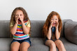 © Lisa Tichané - Little girls sitting on sofa screaming with hands around mouth