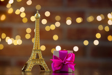 Handmade Gift Box With Purple Bow And Eiffel Tower Golden Souvenir On Wooden Table With Fairy Lights On Bokeh Background