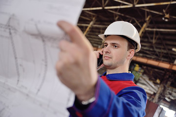 Working engineer in a white construction helmet with a project or drawing plan on the background of an industrial plant