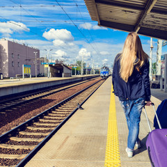 hipster girl with suitcase waiting for train on platform