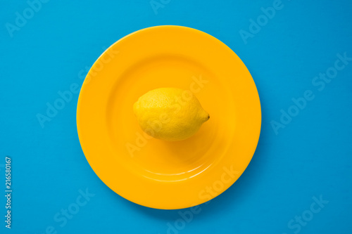 Fotografie, Obraz Top view of lemon on bright yellow plate on blue background/diet concept