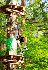 Happy, cute, young boy in white t shirt and helmet having fun and playing at adventure park, holding ropes and climbing wooden stairs. active lifestyle concept