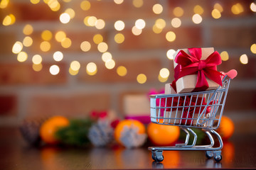 Wall Mural - supermarket cart and gifts on background with fairy lights in bokeh. Christmas Holiday season