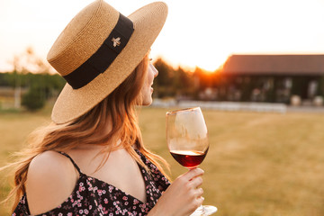 Pretty young woman outdoors holding glass drinking wine.