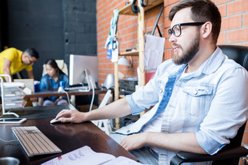 Portrait of modern businessman wearing casual clothes using PC sitting at desk in modern office