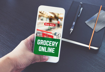 Poster - Hand holding mobile phone and order grocery online for app with promo code with credit card on notebook on black wood table background,Digital marketing concept ,office desk.