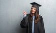 © Krakenimages.com - Young brunette woman over grunge grey wall wearing graduate uniform surprised with an idea or question pointing finger with happy face, number one