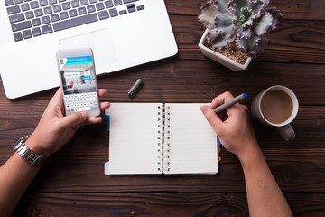 Wall Mural - man using a smartphone for booking hotel online and write something on notebook with wooden desk bac