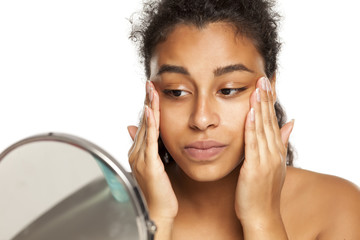 Wall Mural - portrait of a happy young dark-skinned woman applying cream on her face on a white background