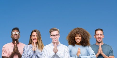 Wall Mural - Composition of group of friends over blue blackground praying with hands together asking for forgiveness smiling confident.