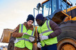 © Seventyfour - Waist up portrait of two industrial workers, one African-American, drinking coffee and using digital tablet standing next to heavy industrial truck on worksite