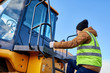 © Seventyfour - Portrait of bearded worker climbing ladder of heavy yellow truck against cold blue sky, copy space