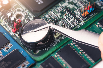 The technician is laying a cr2025 battery on the socket of the computer motherboard. the concept of computer, service, electronics, hardware, repairing, upgrade and technology.