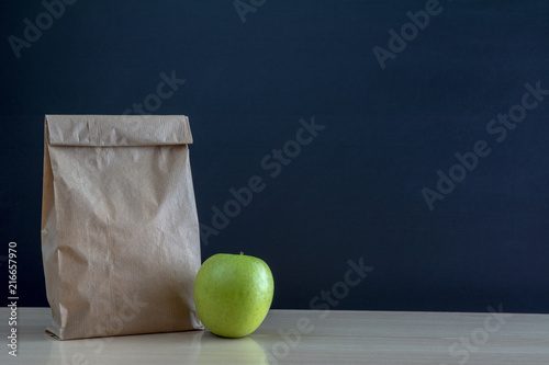 Fotografía Bolsa de almuerzo de papel en el pupitre de la escuela con una manzana verde
