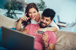 © Mediteraneo - Man using laptop and woman holding credit card. Young couple shopping online with credit card at home