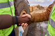 © Seventyfour - Mid section  portrait of two unrecognizable industrial workers wearing reflective jackets shaking hands outdoors