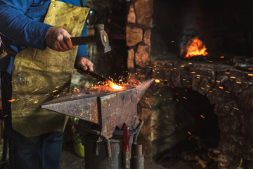 Blacksmith manually forging the molten metal on the anvil in smithy with spark fireworks, close up