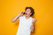 © Drobot Dean - Photo of happy young guy with curly hair shouting and talking on smartphone, isolated over yellow background