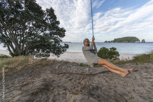 Young Woman Rope Swinging On The Beach And Te Karaka Island