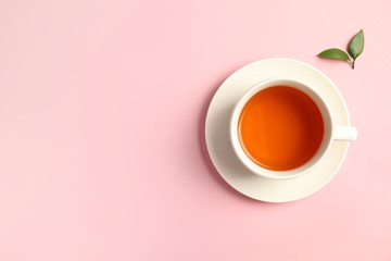 Cup of delicious tea with green leaves on color background, top view