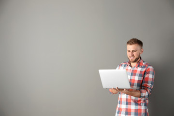 Wall Mural - Young handsome man with laptop on color background