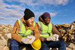 © Seventyfour - Portrait of two industrial  workers wearing reflective jackets, one of them African, relaxing taking break from work  and chatting on mining worksite outdoors