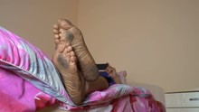 A Young Man With Dirty Feet Is On A Clean Bed And Uses A Mobile Phone.