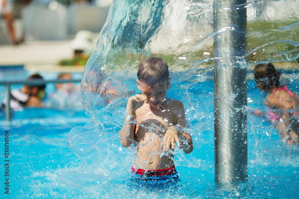 Happy kid playing in blue water of swimming pool on a tropical resort ...