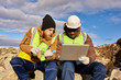 © Seventyfour - Portrait of two industrial  workers wearing reflective jackets, one of them African, using laptop on mining worksite outdoors