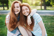 Wanna Hug Her Forever. Portrait Of Happy And Carefree Two Twin Sisters With Natural Red Hair And Freckles, Laughing Out Loud And Cuddling, Fooling Around While Resting In Park On Fresh Green Grass
