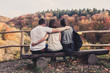Three people hugged each other sitting on wooden benches and watch the beautiful autumn landscape, concept of polygamy