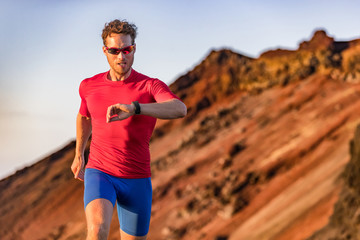 Wall Mural - Athlete runner checking cardio on sports smartwatch jogging on outdoor run track. Running man wearing sunglasses and tech wearable device looking at watch during training workout.