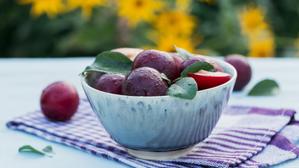 Wall Mural - Fresh plums with leaves in a bowl on white rustic wooden table background.